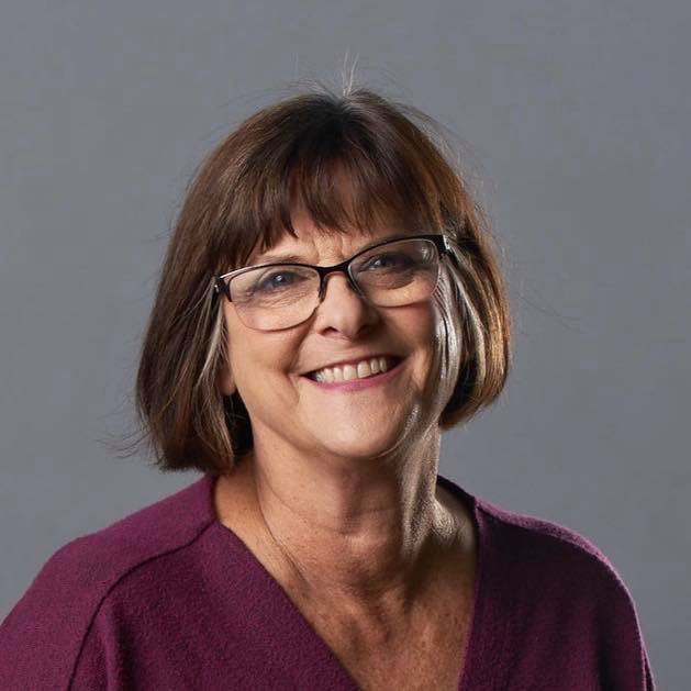 JoAnn-headshot A woman with short brown hair and glasses smiles at the camera. She wears a purple top.
