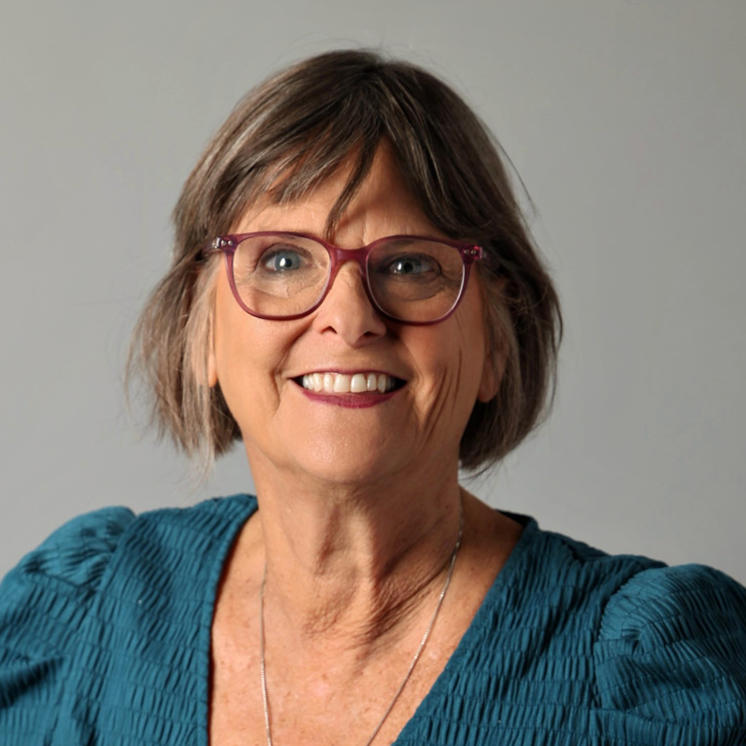 headshot2026 A woman with short brown hair and glasses wearing a teal top smiles at the camera, representing smallbizsk.